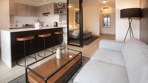 A modern kitchen with wooden cabinets, a bar area with stools, a large mirror, and a sofa in a living area. - Wynwood El Sol Este in Barranco (Lima)