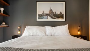 A neatly made bed with white linens, a framed cityscape picture on the wall, and two bedside lamps. - Wynwood El Sol Este in Barranco (Lima)