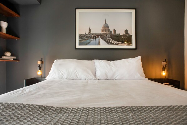 A neatly made bed with white linens, a framed cityscape picture on the wall, and two bedside lamps. - Wynwood El Sol Este in Barranco (Lima)