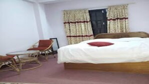A bedroom with a wooden bed, a red pillow, a chair, and a window with curtains. - MeroStay 219 Yam Homestay (Kathmandu)