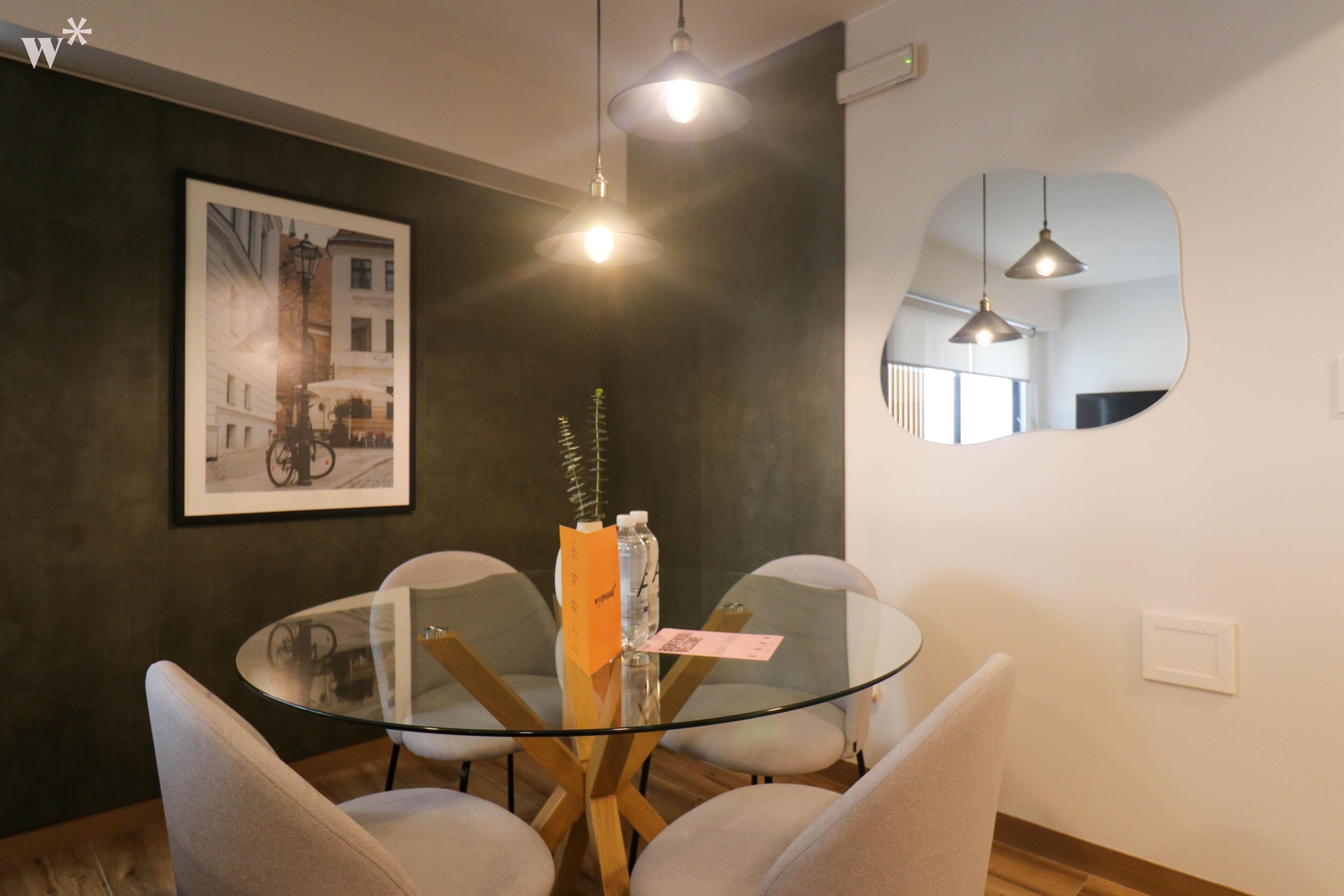 Quarto moderno com uma mesa redonda de vidro, quatro cadeiras, um quadro na parede e um espelho refletindo o ambiente.
