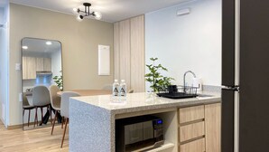 A modern kitchen with a granite countertop, a built-in microwave, and a sink with a black faucet. There are two bottles of water on the counter, and a potted plant beside the sink. - Wynwood Colon in Miraflores (Lima)