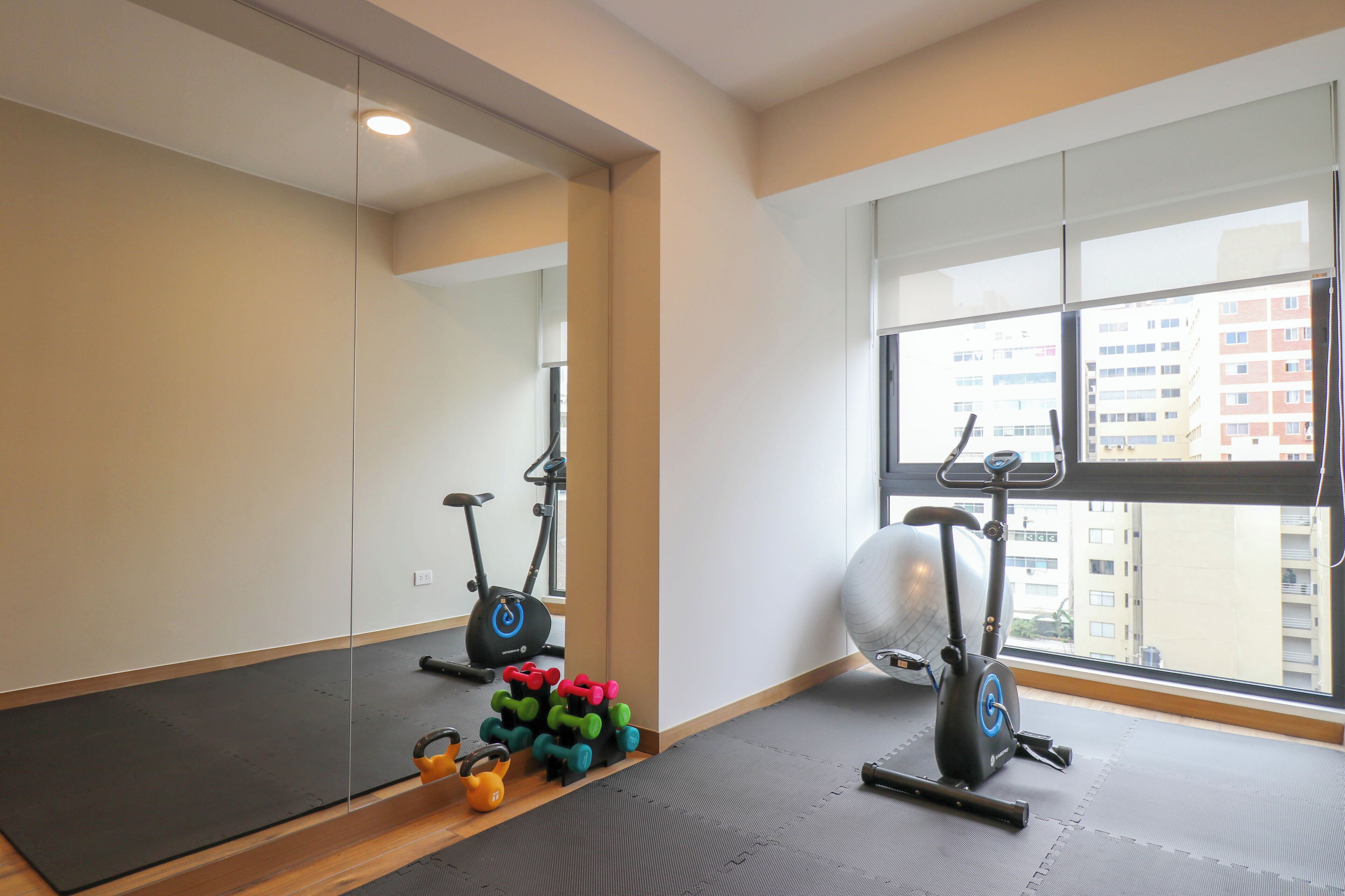 A gym with exercise equipment, a large mirror, and a view of buildings through the window.