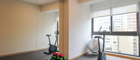 A gym with exercise equipment, a large mirror, and a view of buildings through the window.