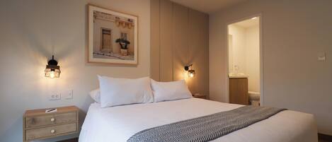 A neatly made bed with a patterned throw, bedside lamps, a framed picture on the wall, and a wooden nightstand.