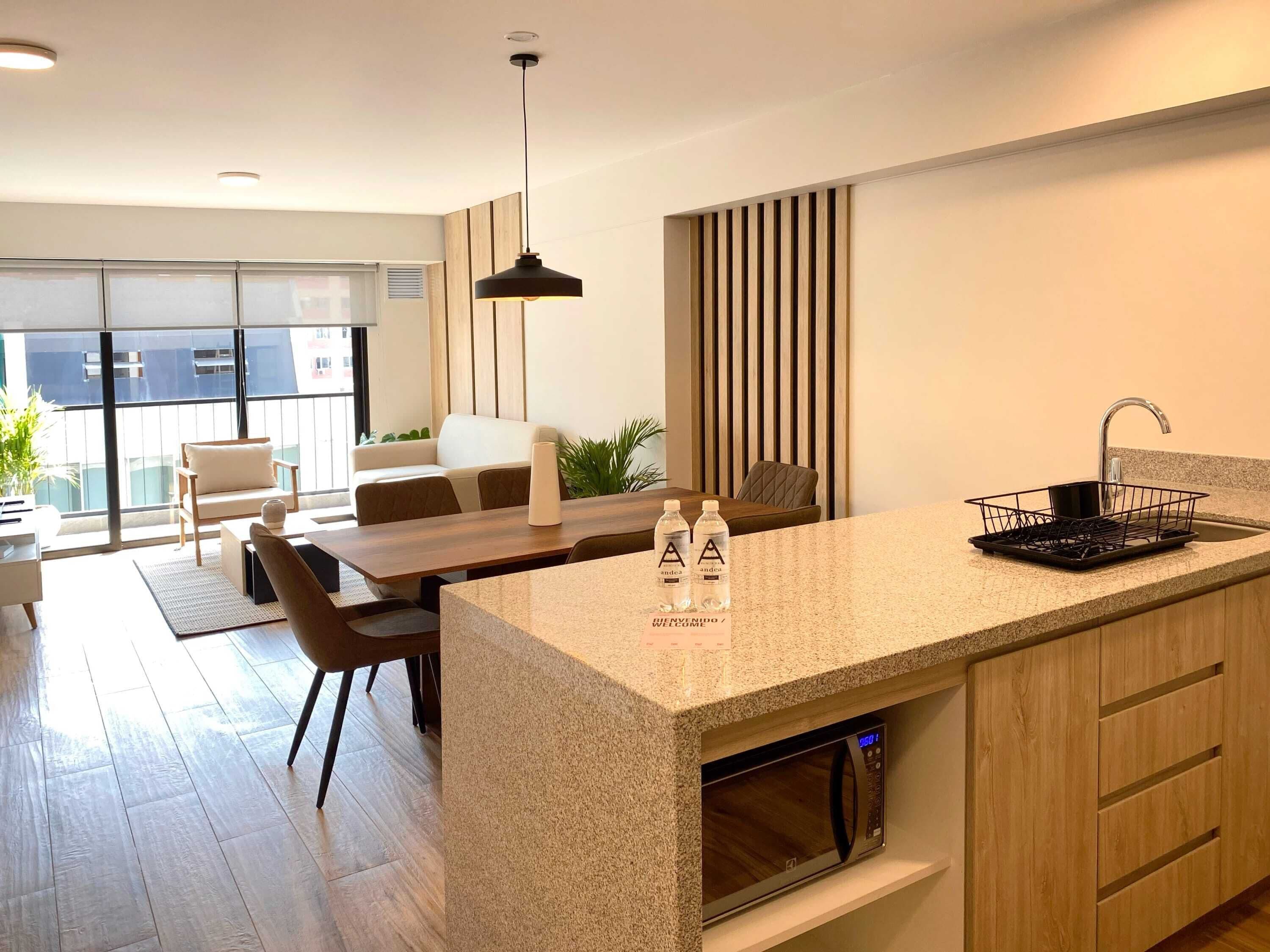 A modern kitchen with a built-in microwave, a sink with a dish rack, and a dining area with a table and chairs.