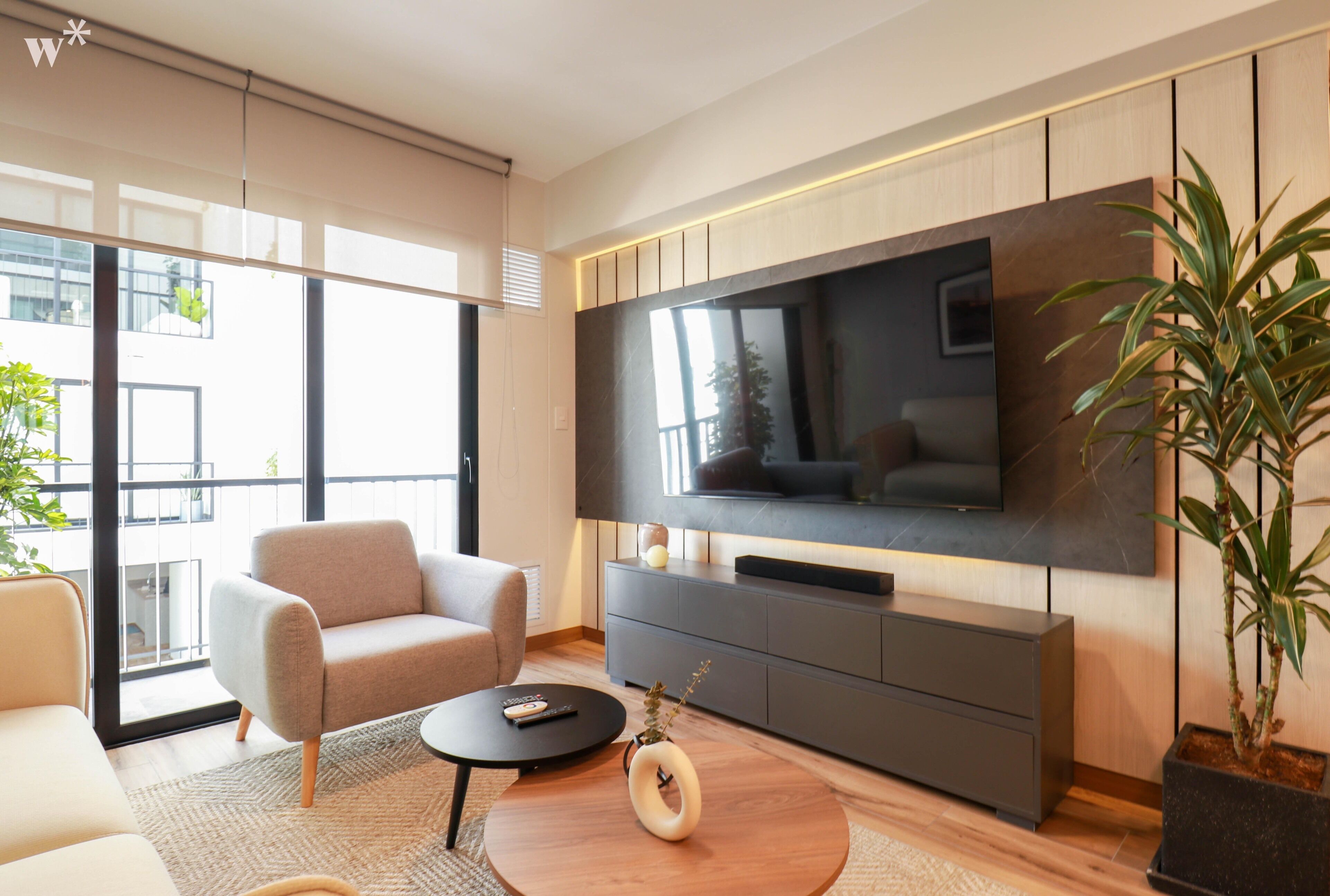 A modern living room with a large flat-screen TV, a sofa, a coffee table, and a potted plant.
