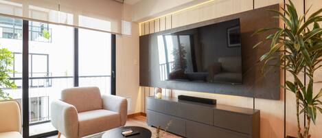 A modern living room with a large flat-screen TV, a sofa, a coffee table, and a potted plant.