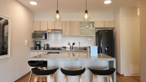 A modern kitchen with a central island, bar stools, a microwave, a coffee maker, and a refrigerator. - Wynwood Colon in Miraflores (Lima)