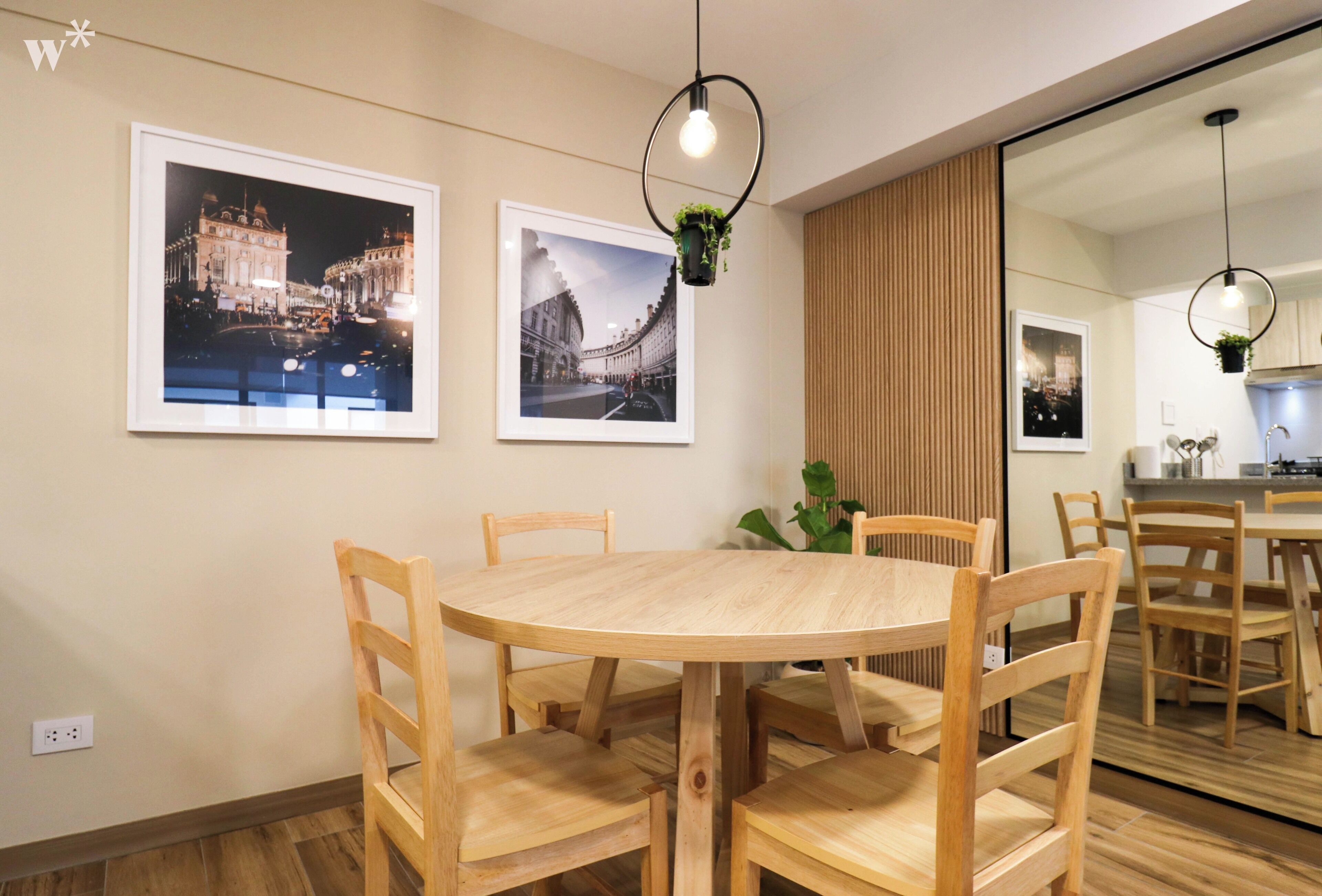 Uma sala de jantar com uma mesa redonda de madeira e cadeiras, duas imagens emolduradas na parede e um lustre.