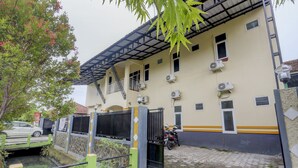 Un edificio con varias unidades de aire acondicionado, un acceso con reja, una motocicleta estacionada en el interior y un pequeño canal de agua en la parte frontal.