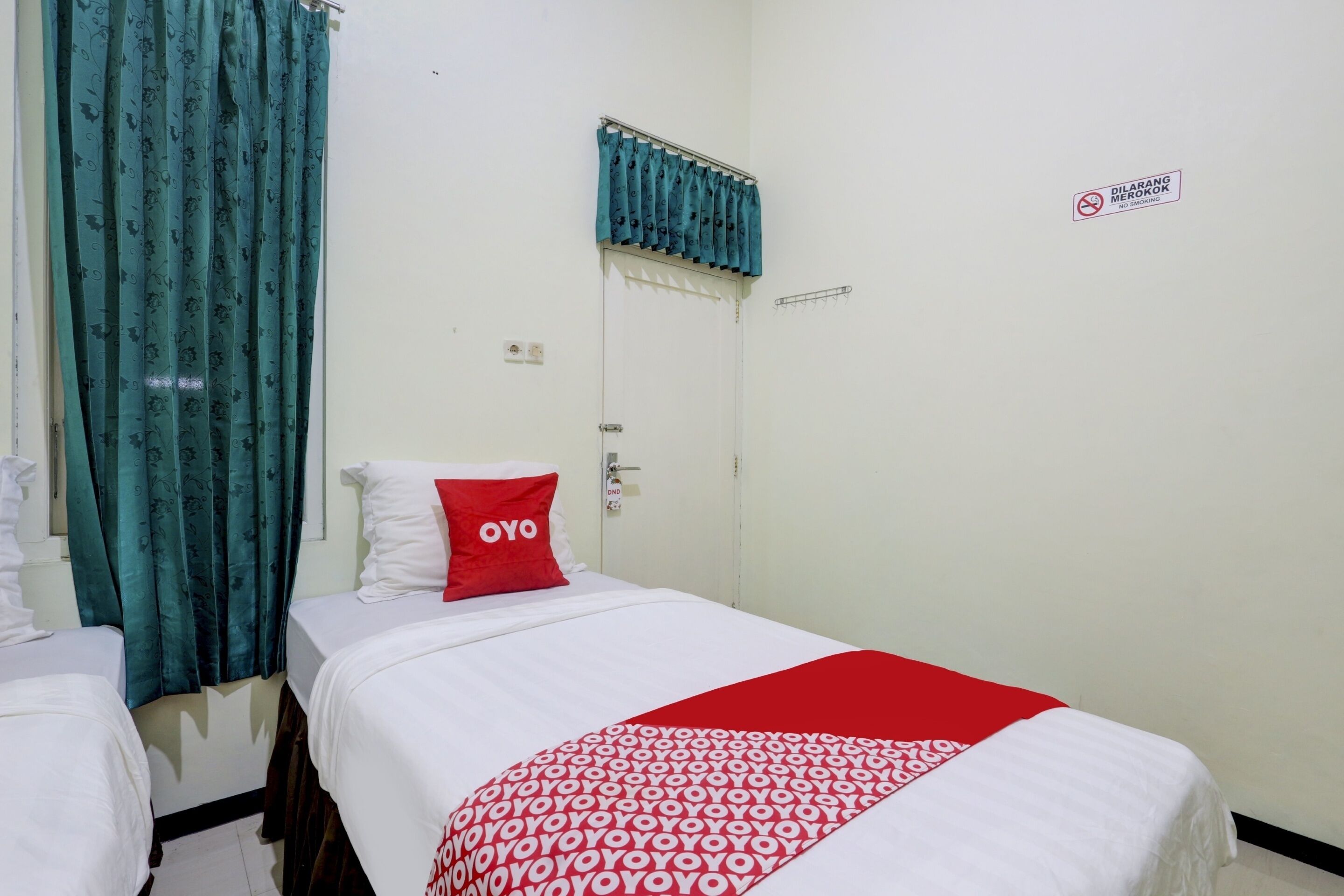 A hotel room with a bed, a red pillow, a white bedspread, and a blue curtain.