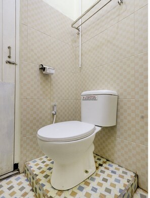 Une petite salle de bain compacte, équipée de toilettes, d’un sèche-mains et d’un porte-rouleau de papier toilette fixé au mur.