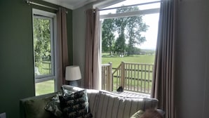 A room with a view of a grassy area and trees through a large window. - Cottage in Brookland near Romney Marsh Beach (Fairfield)
