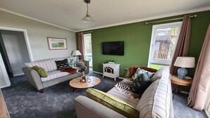 A living room with a sofa, armchair, coffee table, and a TV on the wall. - Cottage in Brookland near Romney Marsh Beach (Fairfield)