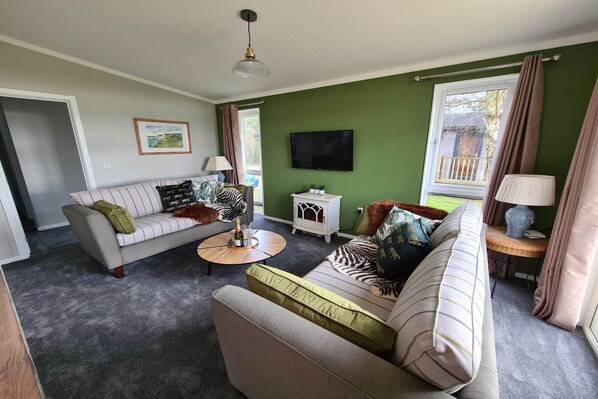 A living room with a sofa, armchair, coffee table, and a TV on the wall. - Cottage in Brookland near Romney Marsh Beach (Fairfield)