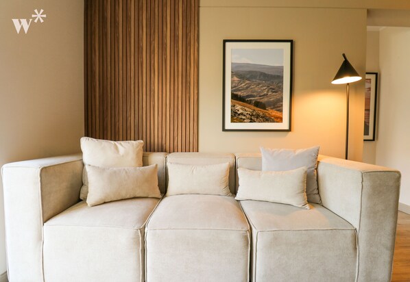 A modern living room with a sectional sofa, a framed landscape painting, and a floor lamp.