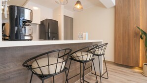 A modern kitchen with a coffee maker, two bar stools, pendant lights, and a wooden cabinet. - Wynwood Dean Valdivia (Lima)