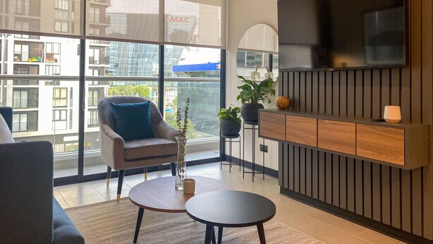 A modern living room with a large TV, comfortable seating, and a view of the city through floor-to-ceiling windows. - Wynwood Rivera Navarrete (Lima)
