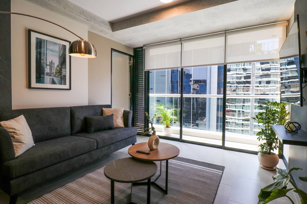 Ein modernes Wohnzimmer mit einer Couch, einem Couchtisch, einer Lampe und einem großen Fenster mit Blick auf die Stadt.