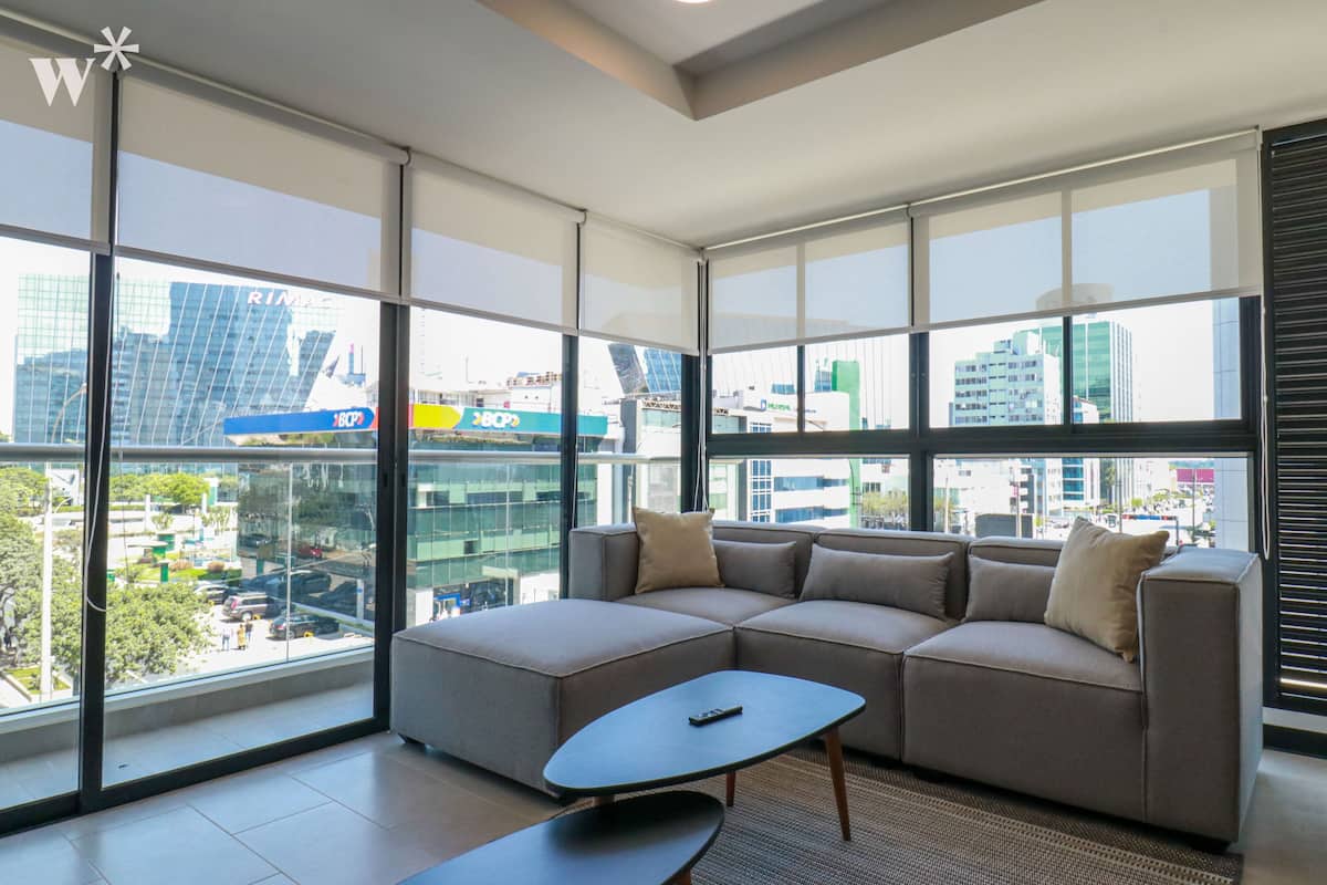 Ein modernes Wohnzimmer mit einer Eckcouch und einem Couchtisch, große Fenster mit Blick auf die Stadt.