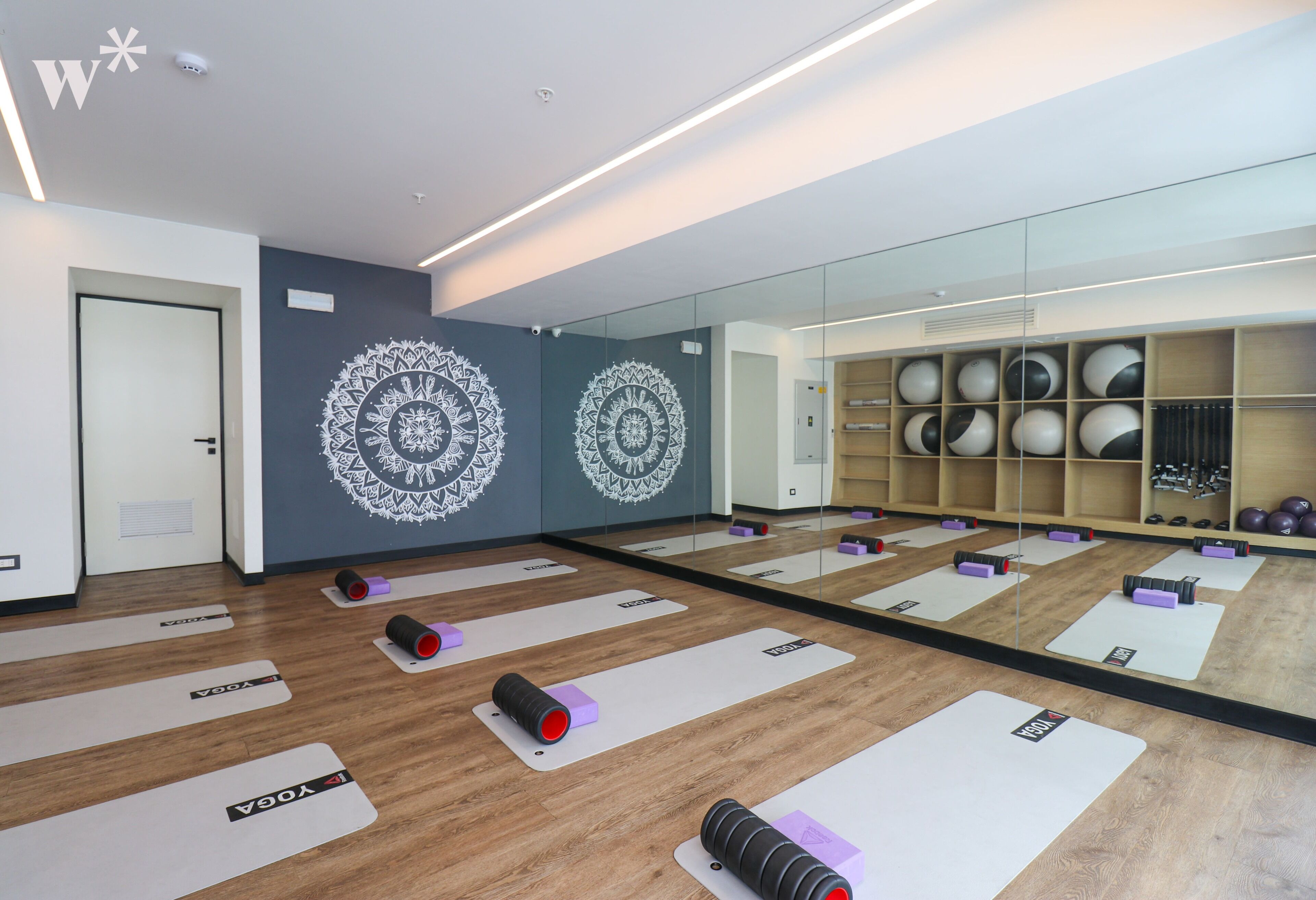 Une salle de sport moderne dotée d’un plancher en bois, de murs recouverts de miroirs et de tapis de yoga.