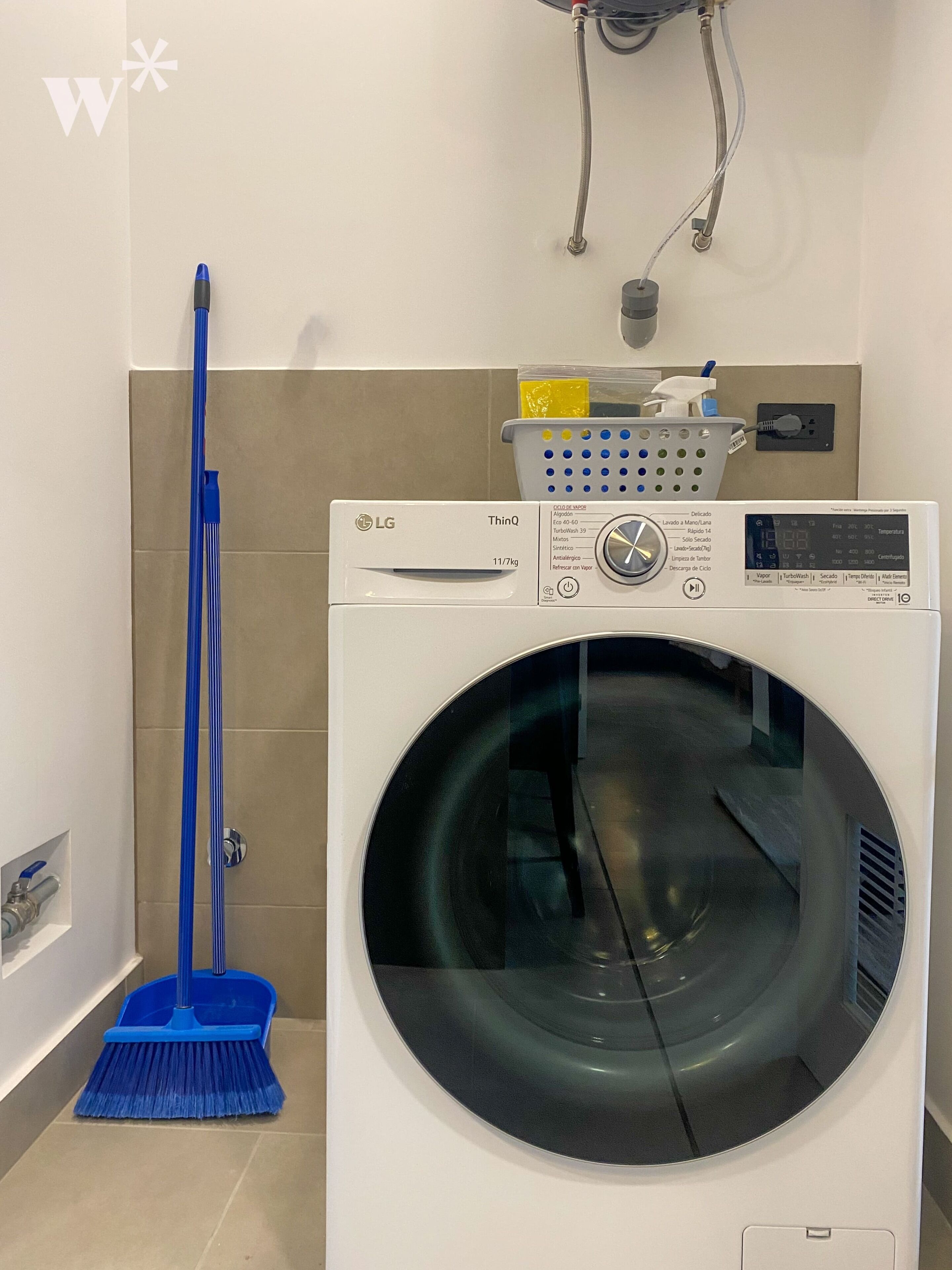 A laundry room with a front-loading LG ThinQ washer and dryer, a blue mop, and a wall-mounted laundry basket.
