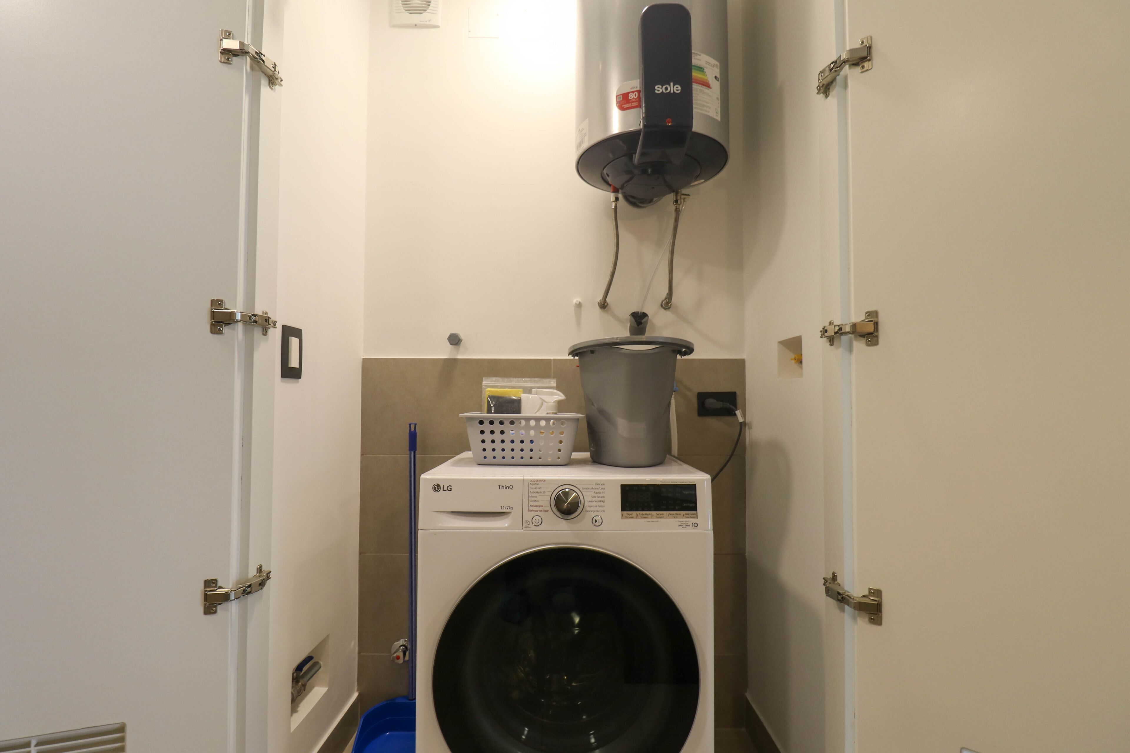 A compact laundry room with a front-loading washing machine, a drying machine, and a wall-mounted heater.