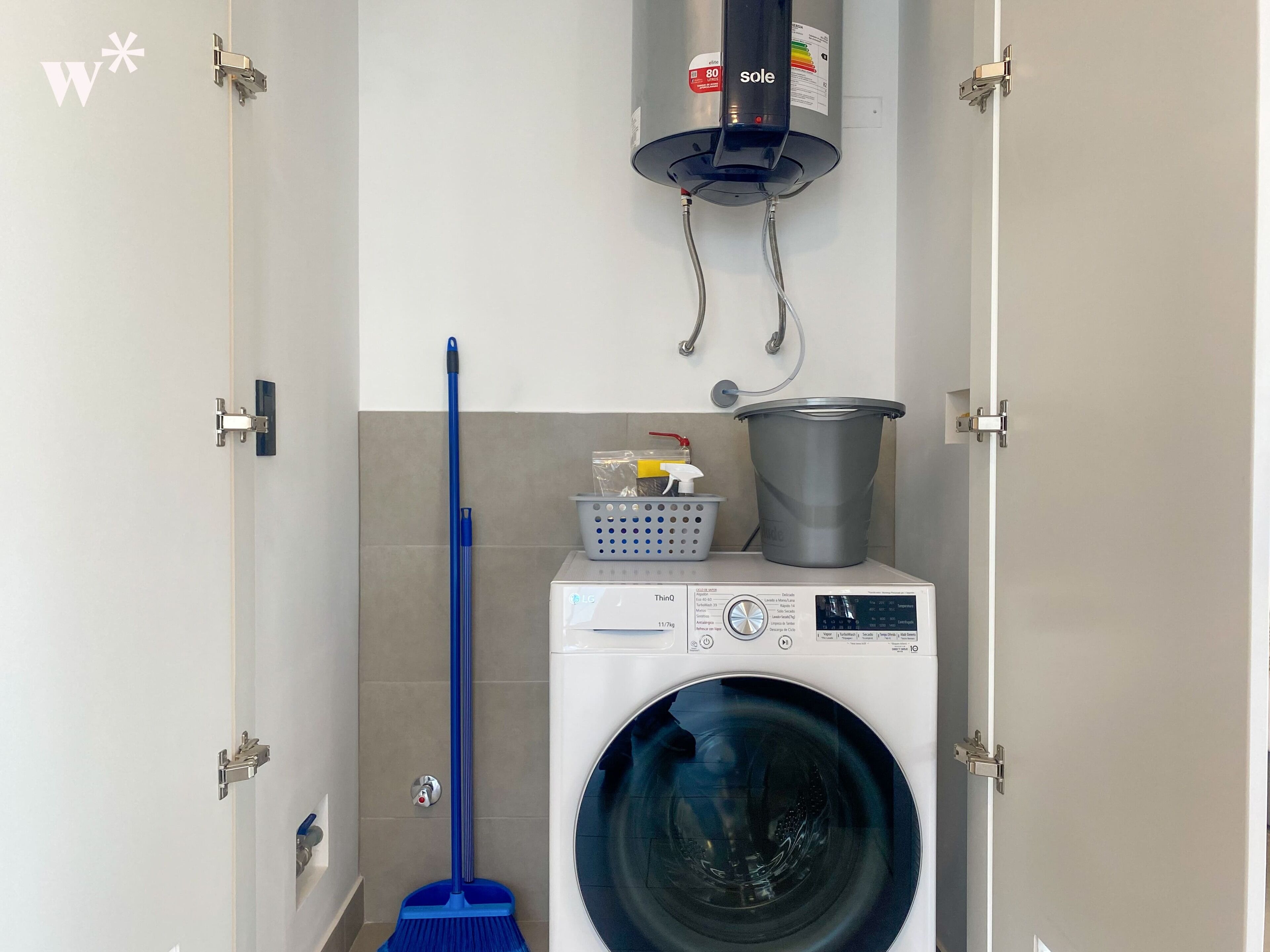 A compact laundry room with a front-loading washing machine, a mop, a bucket, and a water heater.