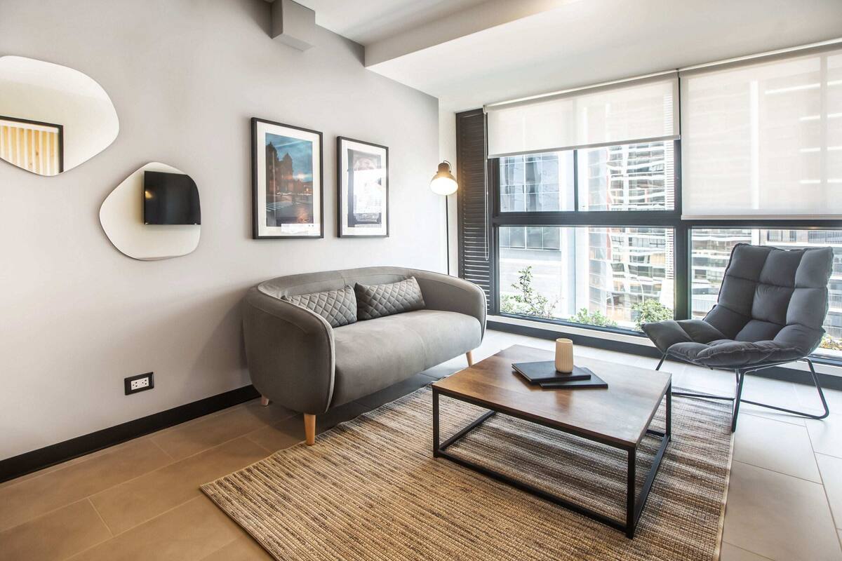 Ein modernes Wohnzimmer mit grauem Sofa, einem schwarzen Sessel, einem Couchtisch und gerahmten Bildern an der Wand.