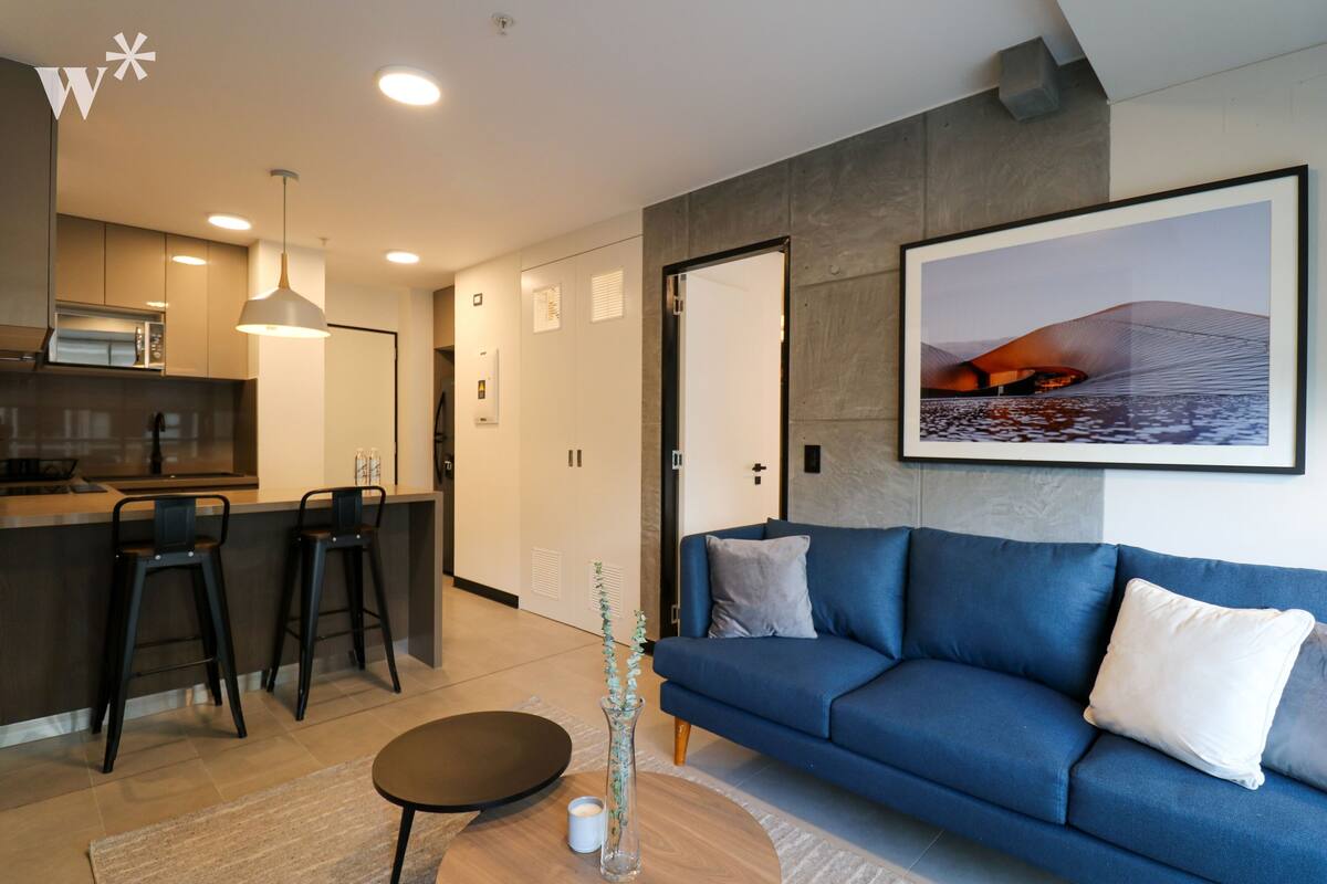 Ein modernes Wohnzimmer mit einem blauen Sofa, einem Couchtisch und einer Küchenzeile mit Barhocker.