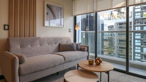 A modern living room with a grey sofa, a round wooden coffee table, and a large window offering a view of a cityscape. - Wynwood Rivera Navarrete (Lima)