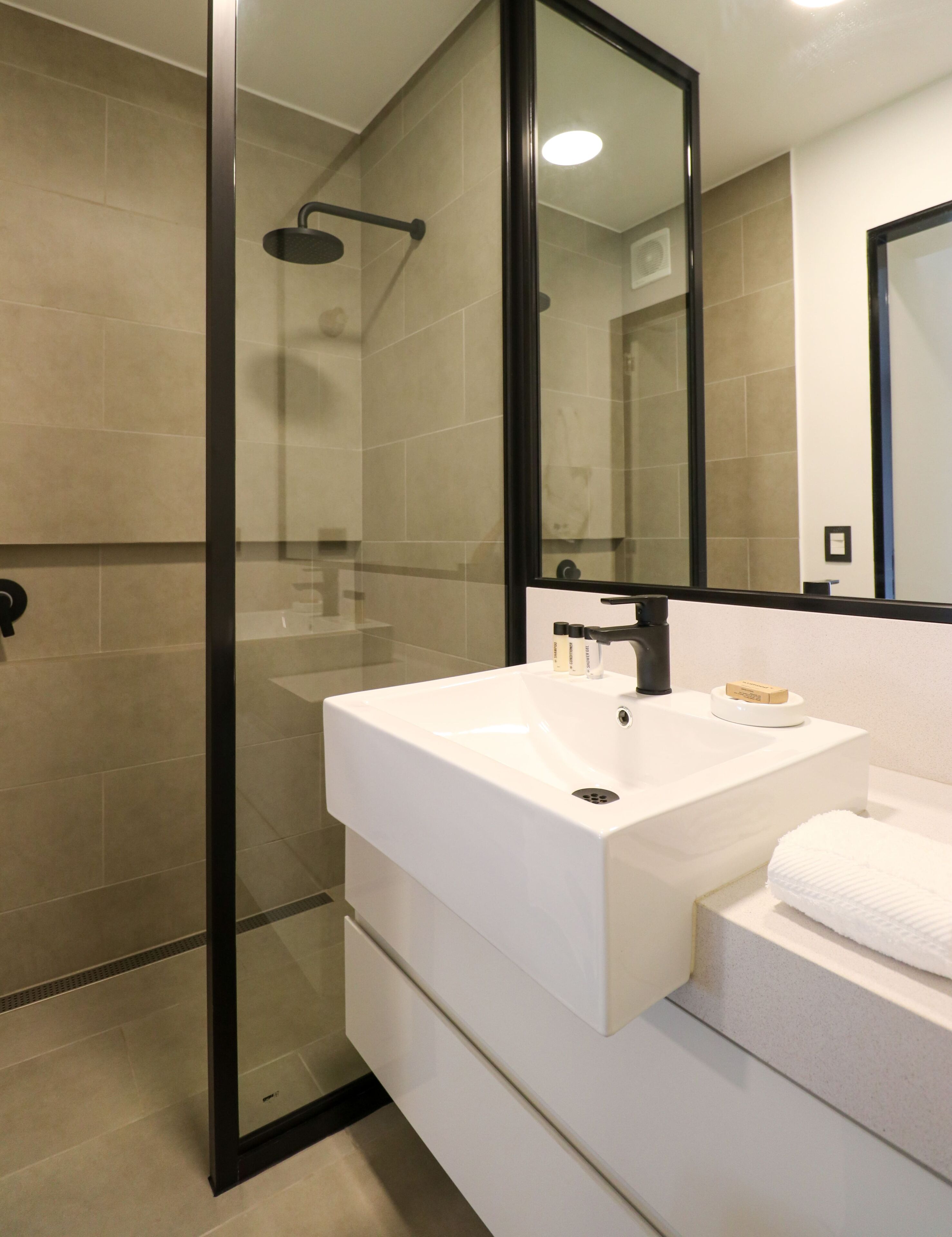 Un bagno moderno con doccia a vetro, un lavandino bianco con portasapone e uno specchio grande.