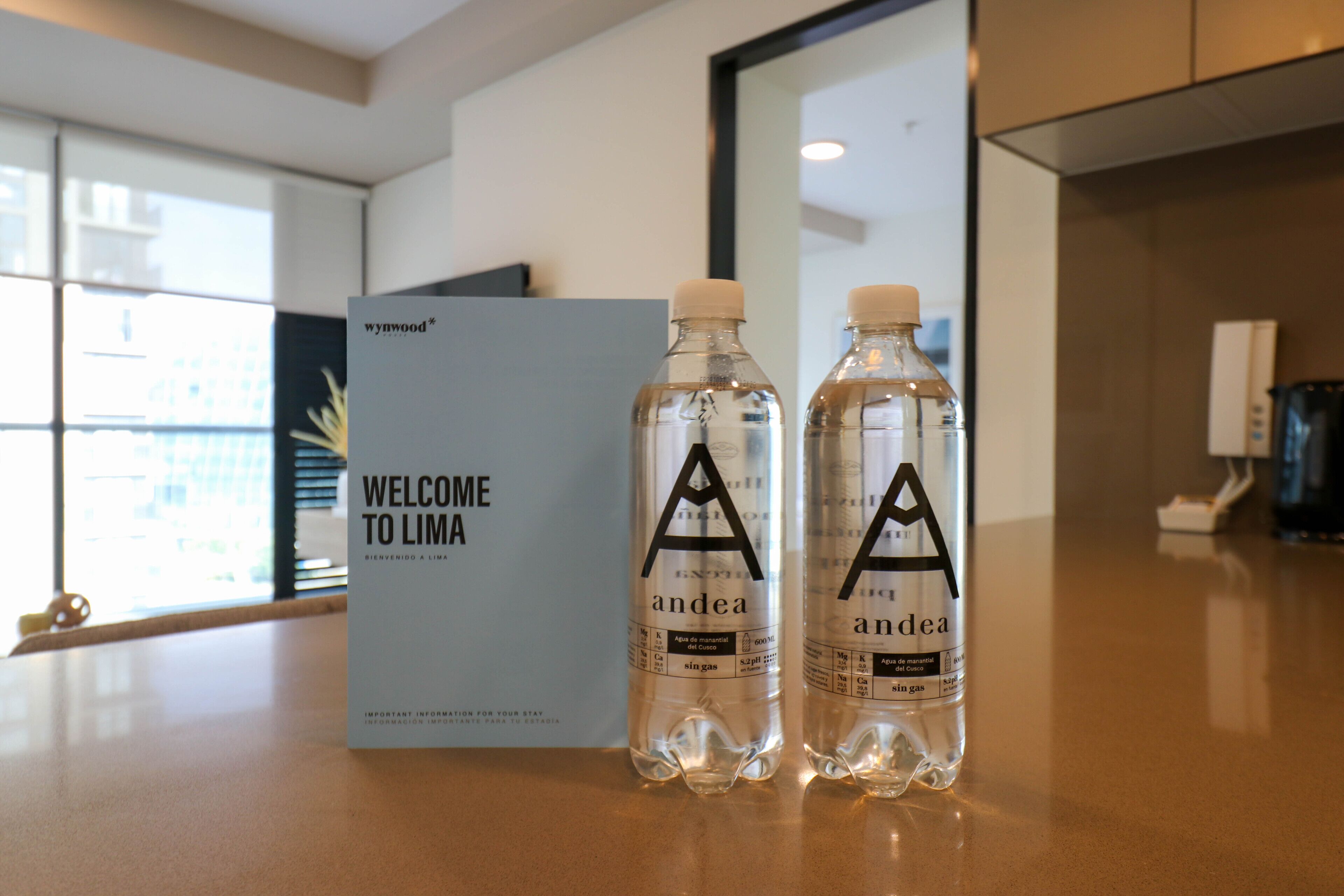 Dos botellas de agua con etiquetas y un cartel de bienvenida en un moderno vestíbulo de hotel.