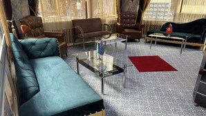 A spacious living room with a large teal sofa, a brown leather armchair, a glass coffee table, and a red rug. - Metropol Hotel 2 (Istanbul)