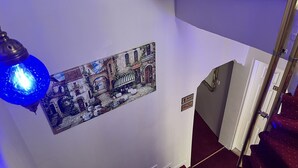 A staircase with a red carpet, a wall-mounted light fixture, and a mural of a street scene. - Metropol Hotel 2 (Istanbul)