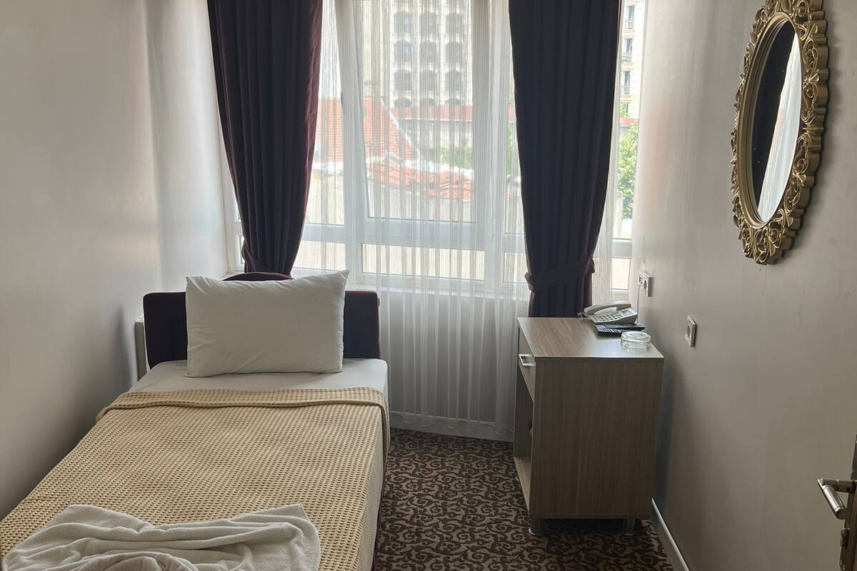 A hotel room with a bed, a desk, a mirror, and a patterned carpet.