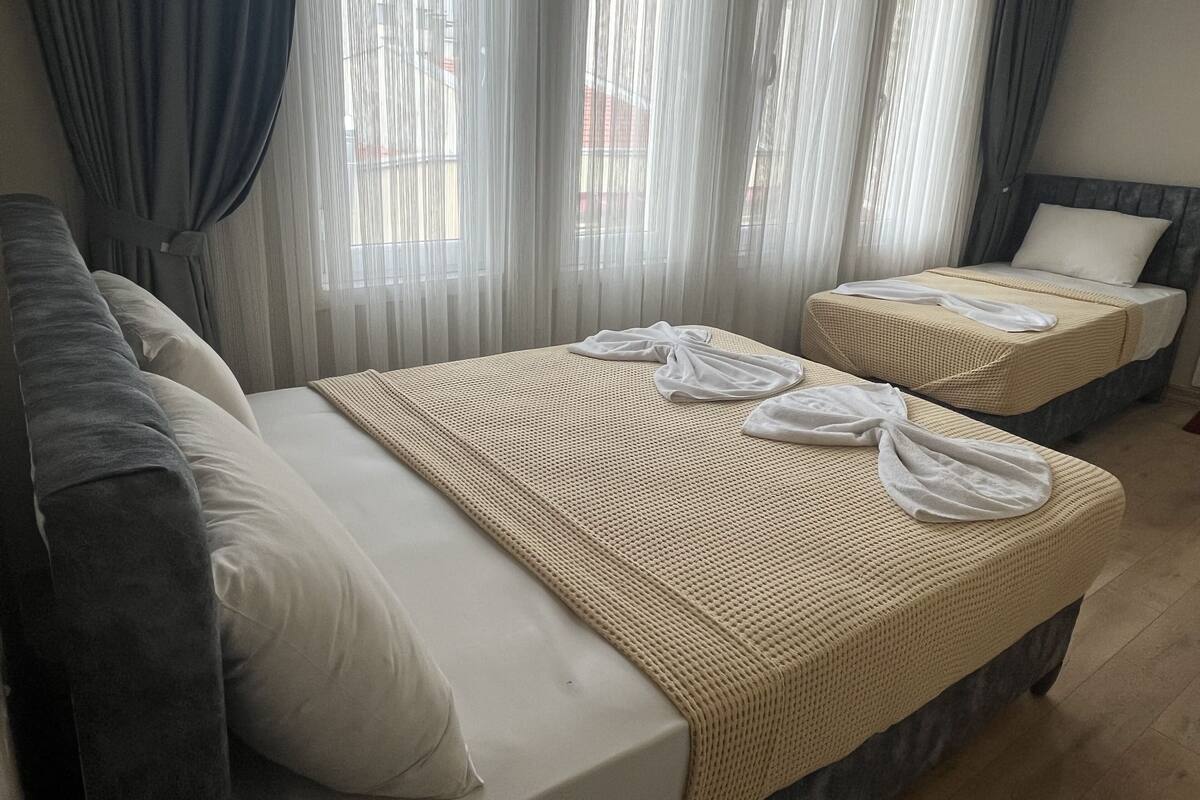 A hotel room with two beds, a sofa, and sheer curtains.