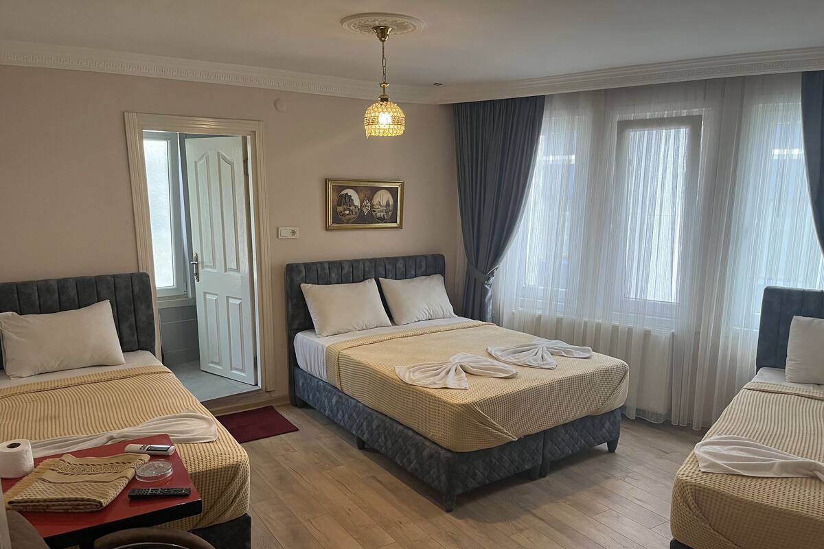 A hotel room with two beds, a sitting area with a table, and a large window with curtains.