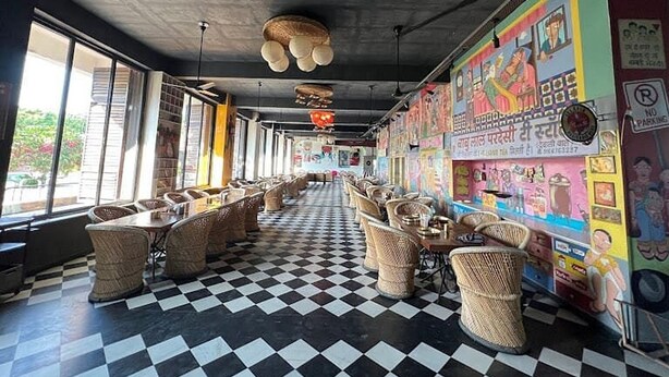 Een restaurant met geruit vloer, rieten meubels en kleurrijke muurschilderingen.