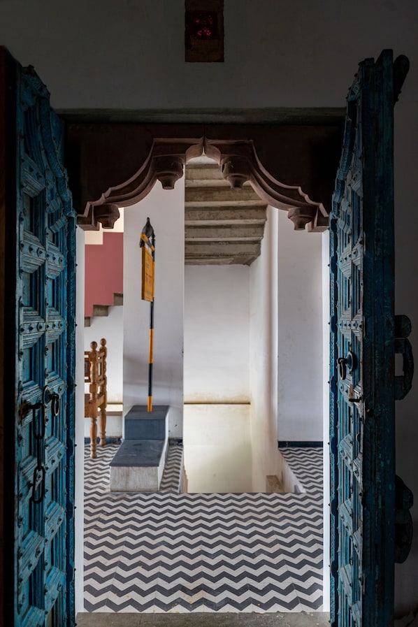 An interior view of a room with a patterned floor, a wooden bench, and a door with intricate blue designs.