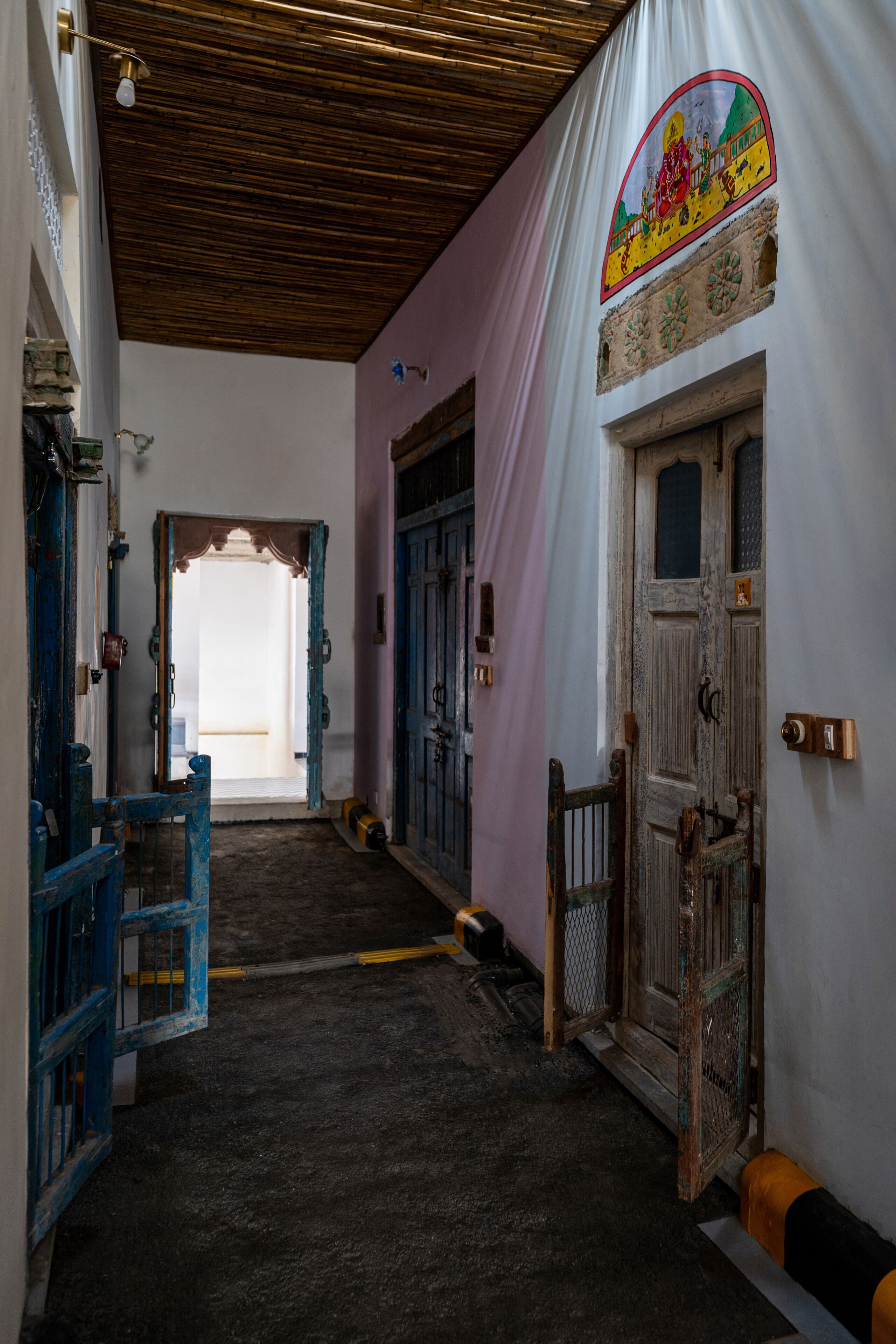 A narrow hallway with a wooden ceiling, a blue chair, and a door with a decorative frame.