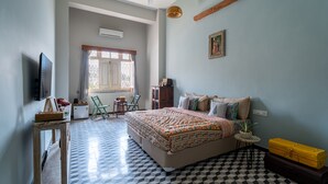 Een slaapkamer met een zwart-wit geruite vloer, een bed met beddengoed met een patroon, een televisie aan de muur en een raam met gordijnen.