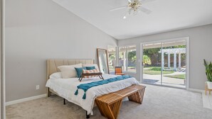 Une chambre avec un lit, un banc, un ventilateur de plafond et de grandes portes coulissantes en verre donnant sur une terrasse.