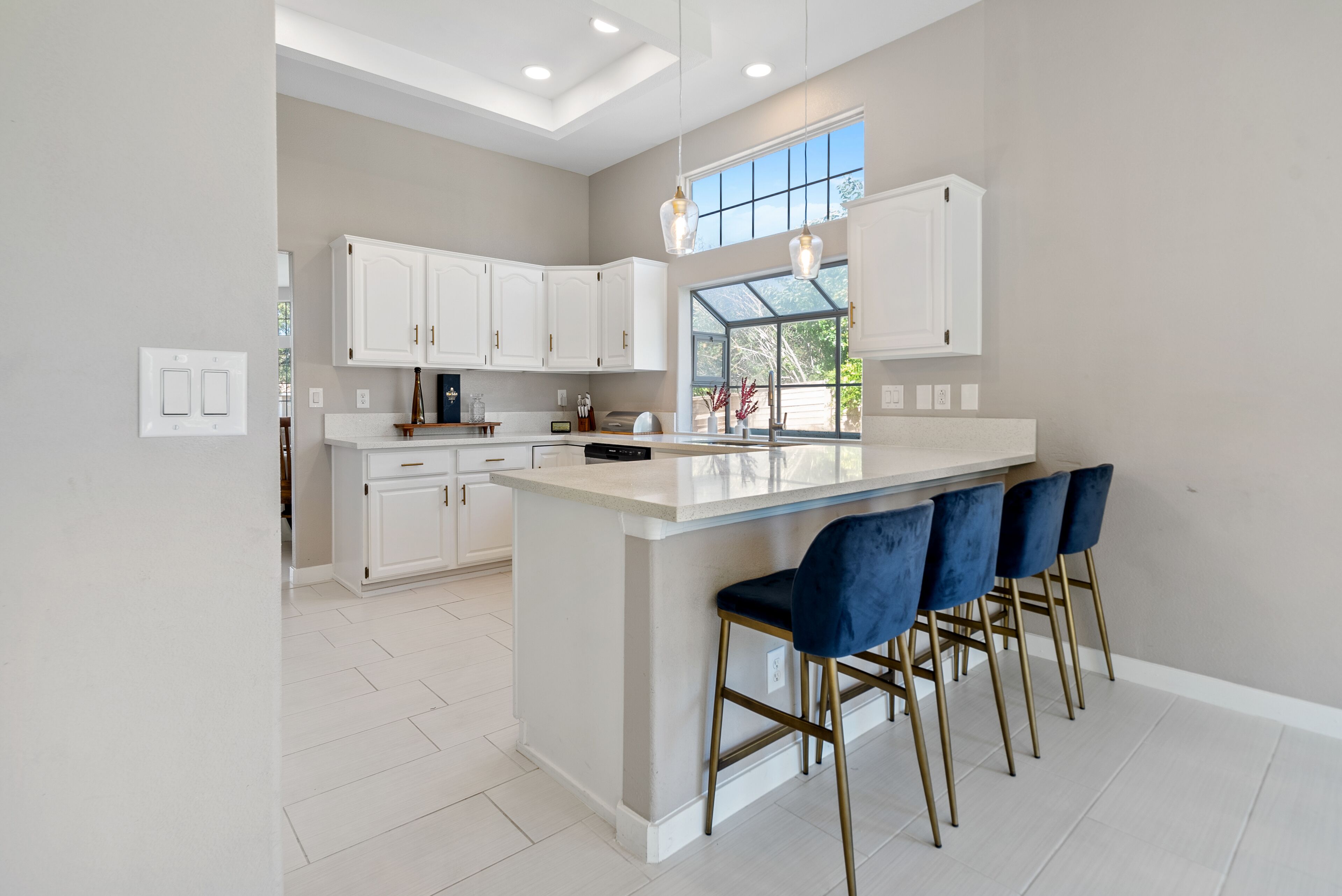 A modern kitchen with white cabinets, a large island with bar stools, and pendant lighting.