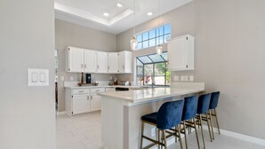 Une cuisine moderne avec des meubles blancs, un grand îlot central doté de tabourets et un éclairage suspendu.