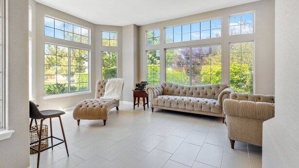 Un salon spacieux avec de grandes fenêtres, un canapé beige, un fauteuil et une petite table.