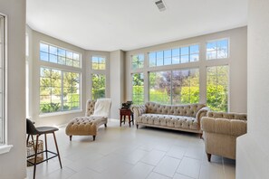 Un salón amplio con ventanas grandes, un sofá color beige, una silla y una mesita.
