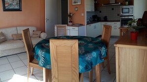Un comedor con mesa y sillas de madera, un sofá y una cocina al fondo.