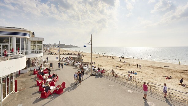 Un paseo marítimo frente a la playa, con mesas al aire libre y vistas al mar.